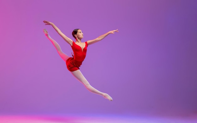 Eine junge Ballerina in einem roten Trikot führt einen Split-Sprung auf einem lila Hintergrund durch