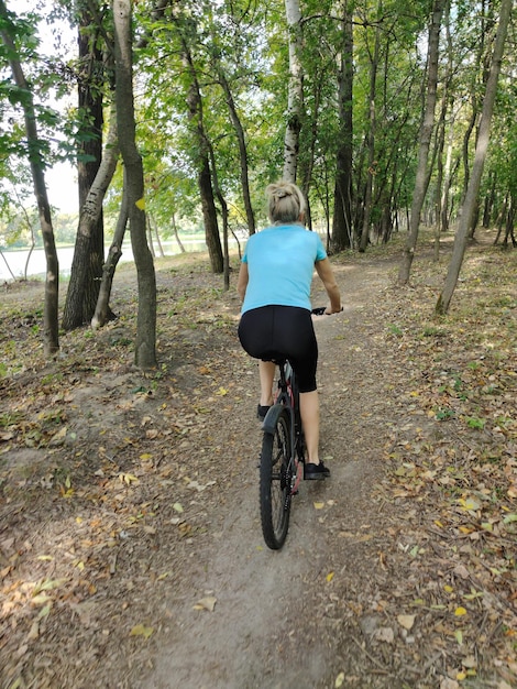 Foto eine junge blonde frau fährt mit dem fahrrad im park auf einem pfad rückwand tourismus, sport und outdoor