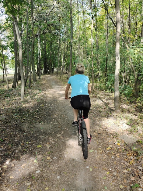 Eine junge blonde Frau fährt mit dem Fahrrad im Park auf einem Pfad Rückwand Tourismus, Sport und Outdoor