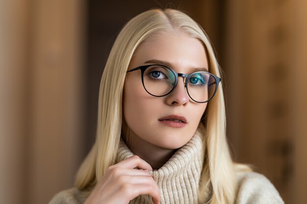 Eine junge blonde Frau in einem Strickpullover sitzt in einem gemütlichen Café