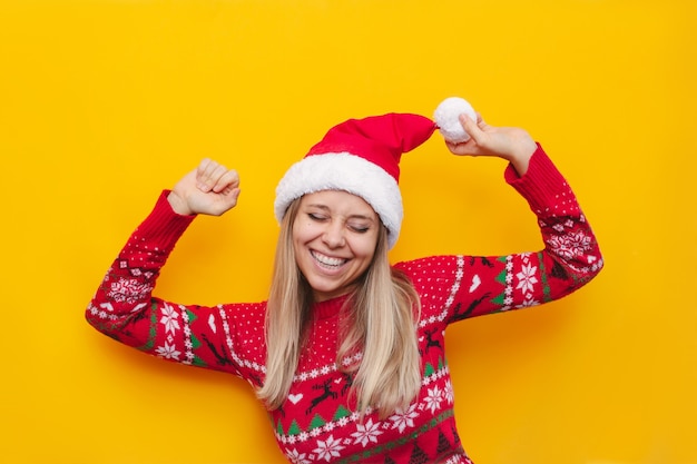Eine junge blonde Frau in einem warmen Rotwildpullover und einer Weihnachtsmannmütze freut sich mit erhobenen Händen