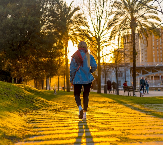 Eine junge Blondine auf dem Rücken mit einer Jacke, die durch die Straßen von Bilbao geht