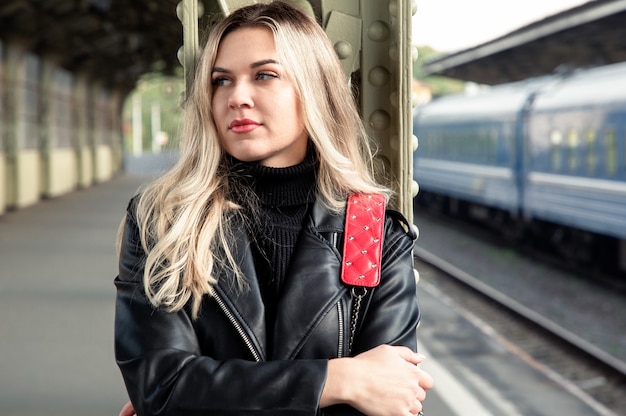 Eine junge Blondine, die an einem Bahnhof an einer Stange lehnt