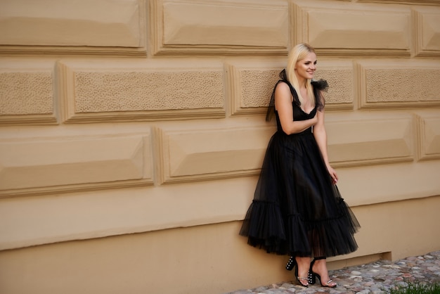 Eine junge Blondine steht in einem schwarzen Kleid in der Nähe eines alten Gebäudes