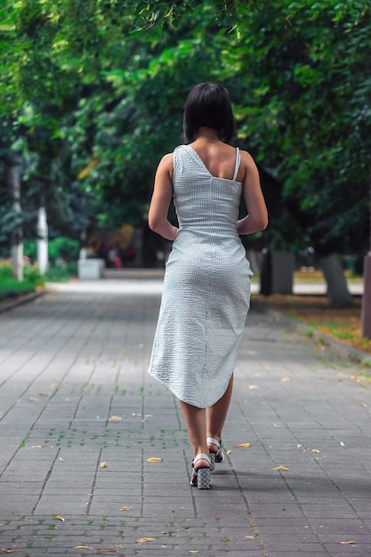 Eine junge brünette Frau mit einer schönen Figur in einem engen Kleid geht durch den Stadtpark