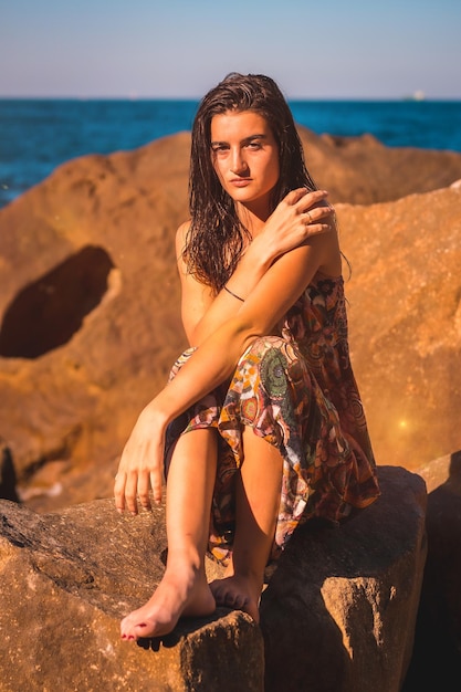 Eine junge Brünette mit nassen Haaren und einem geblümten Kleid am Meeressommer llifestyle