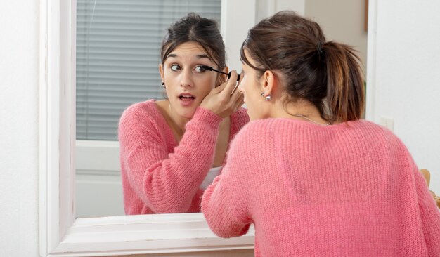 Eine junge Brunettefrau, die Make-up in den Spiegel einsetzt