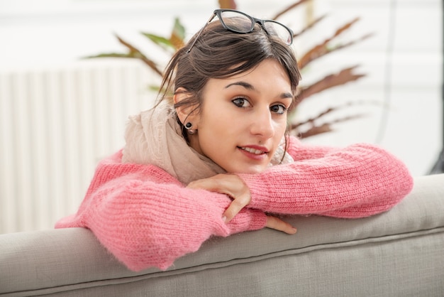 Eine junge Brunettefrau mit der rosa Strickjacke, die auf dem Sofa stillsteht