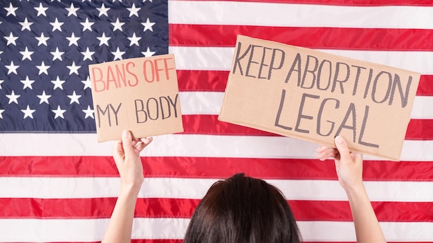 Foto eine junge demonstrantin hält pappe mit den schildern „keep abortion legal“ und „bans of my body“ mit der us-flagge in der hand