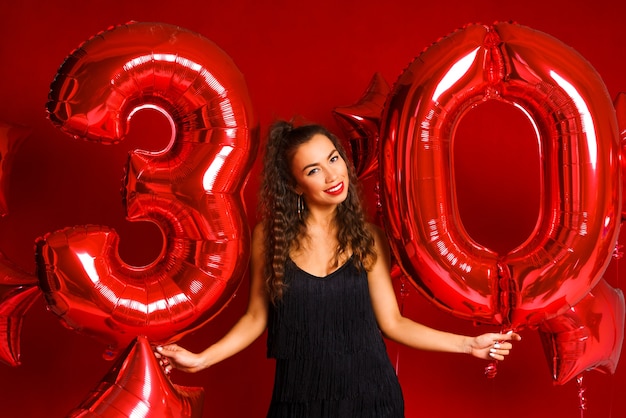 Eine junge erwachsene frau auf einem hintergrund von roten luftballons in form der nummer dreißig modell brunett...