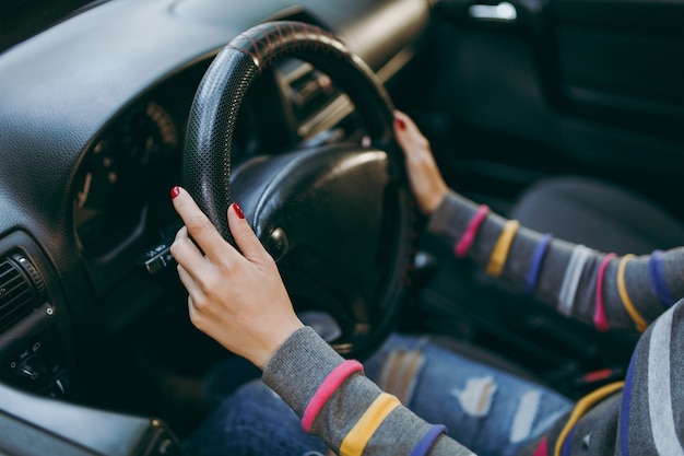 Foto eine junge europäerin mit gesunder, sauberer haut legte ihre hände mit roter maniküre auf ihre nägel auf das lenkrad des autos mit schwarzem interieur. reise- und fahrkonzept.
