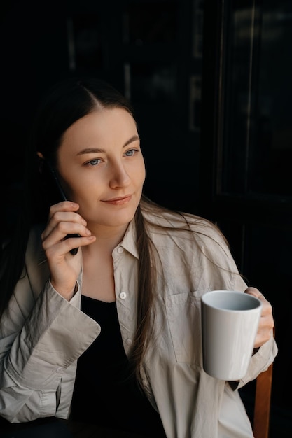 Eine junge europäische Freiberuflerin mit langen dunklen Haaren trinkt Kaffee und arbeitet aus der Ferne in einem Café