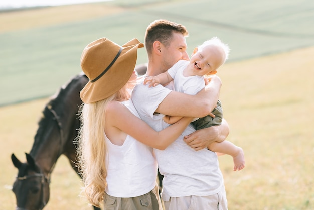 Eine junge Familie hat Spaß auf dem Feld. Eltern und Kind mit einem Pferd