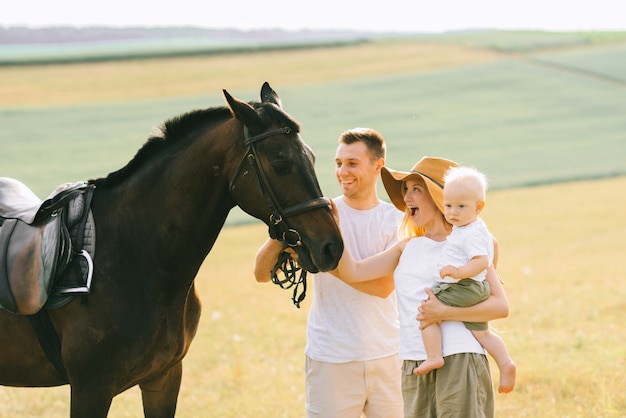 Eine junge Familie hat Spaß auf dem Feld. Eltern und Kind mit einem Pferd