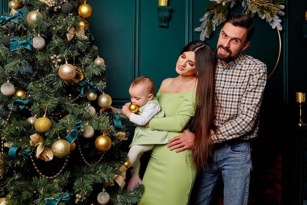 Eine junge Familie mit einem Baby in der Nähe des Weihnachtsbaums Eine Mutter hält ihre kleine Tochter in ihren Armen