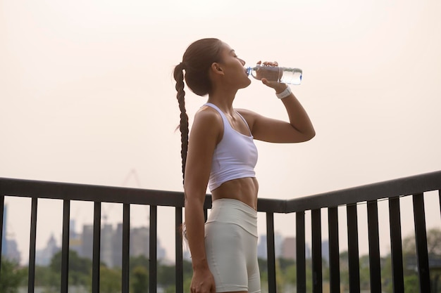 Eine junge Fitnessfrau in Sportkleidung trinkt Wasser im Stadtpark Gesund und Lebensstil