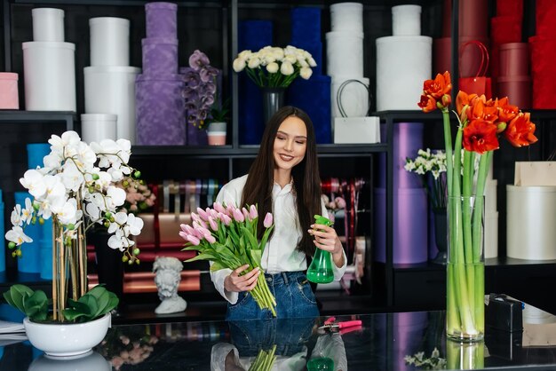 Eine junge Floristin kümmert sich um Blumen in einem gemütlichen Blumenladen und sammelt Blumensträuße Floristik und Herstellung von Eimern in einem Blumenladen Kleines Unternehmen