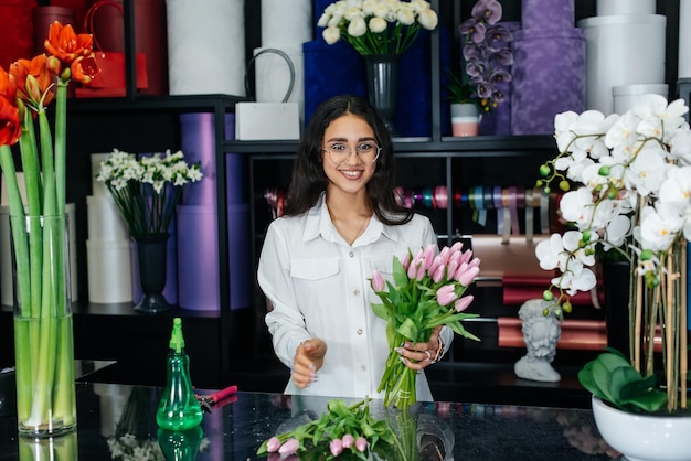 Eine junge Floristin kümmert sich um Blumen in einem gemütlichen Blumenladen und sammelt Blumensträuße Floristik und Herstellung von Eimern in einem Blumenladen Kleines Unternehmen