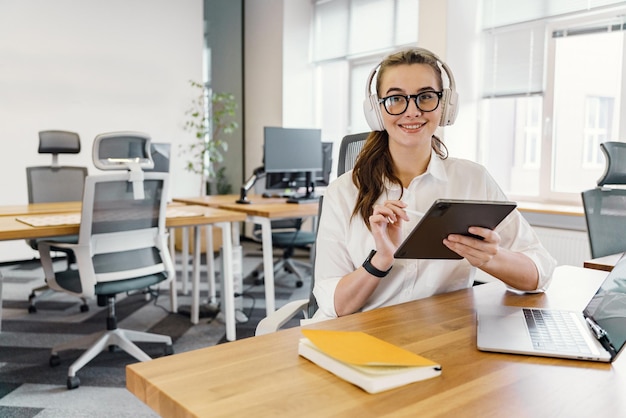 Eine junge Frau arbeitet in einem Coworking-Space, benutzt ein Tablet und einen Laptop.