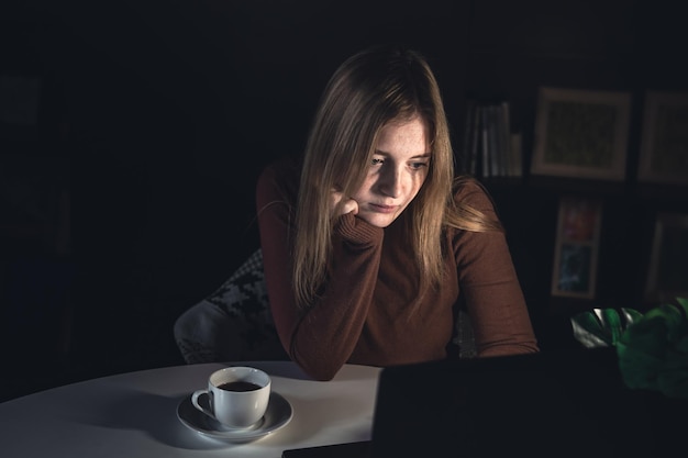 Eine junge Frau arbeitet nachts hinter einem Laptop mit Lampenlicht