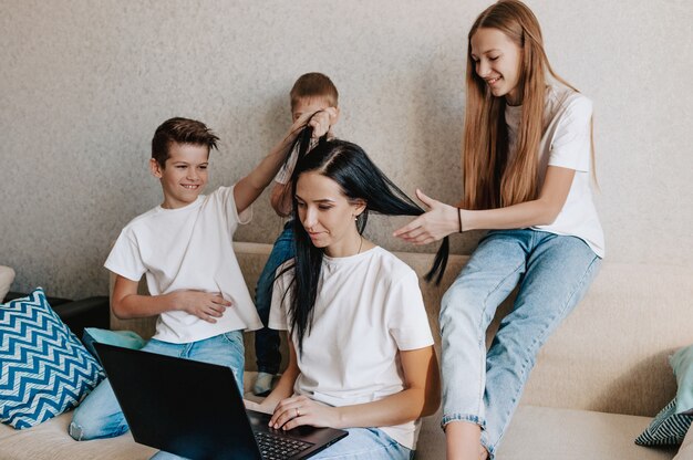 Eine junge Frau arbeitet zu Hause mit einem Laptop zusammen mit den Kindern, die Kinder mit ihrer Mutter kommunizieren wollen, machen Lärm und stören die Arbeit