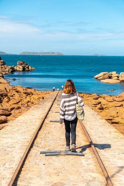 Eine junge Frau auf dem Weg zum Abstieg der Boote neben dem Leuchtturm Mean Ruz, Hafen von Ploumanach, in der Stadt Perros-Guirec, Cotes-d'Armor, in der französischen Bretagne, Frankreich.