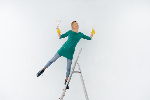 Eine junge Frau auf der Treppe malt eine weiße Wand mit einer Walze