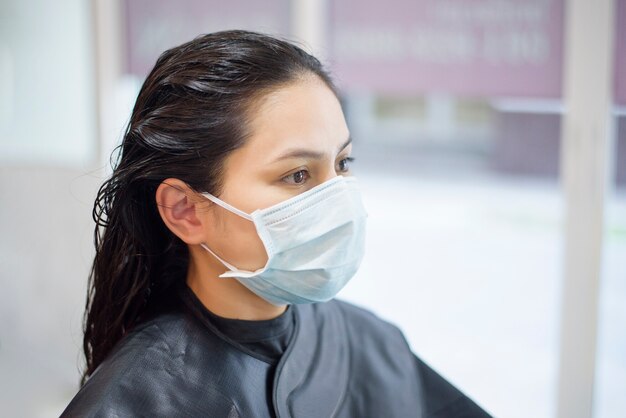 Eine junge Frau bekommt einen Haarschnitt in einem Friseursalon und trägt eine Gesichtsmaske