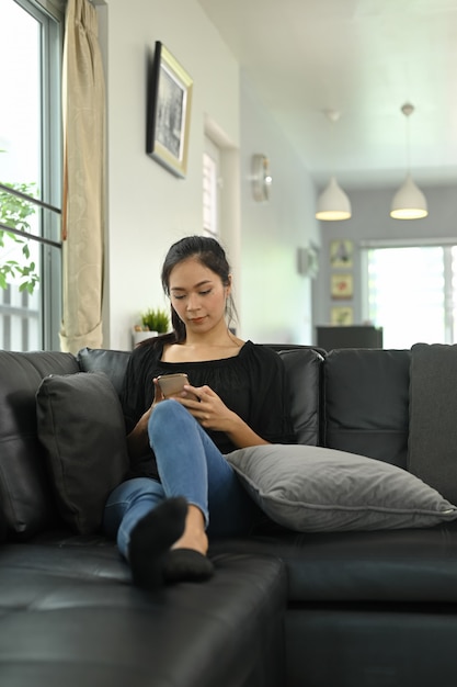 Eine junge Frau benutzt ein Smartphone, während sie auf einem Ledersofa sitzt