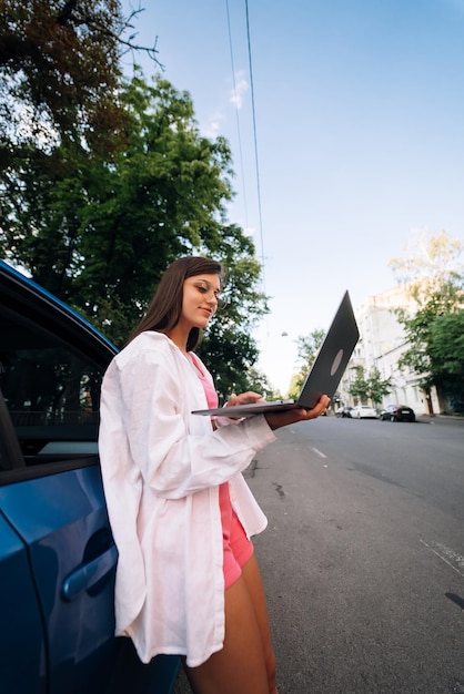 Eine junge Frau benutzt einen Laptop in der Nähe eines Autos