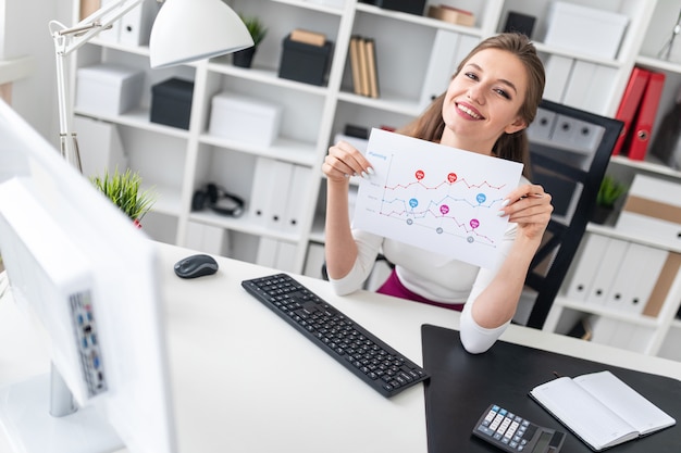 Eine junge Frau, die an einem Computertisch sitzt und ein Blatt mit Diagrammen hält.