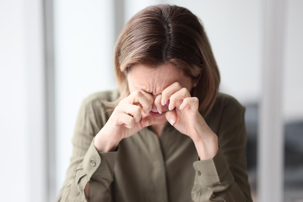 Eine junge Frau, die an einem Tisch im Büro sitzt, wischt sich die Augen ab und ermüdet sich in der Nähe