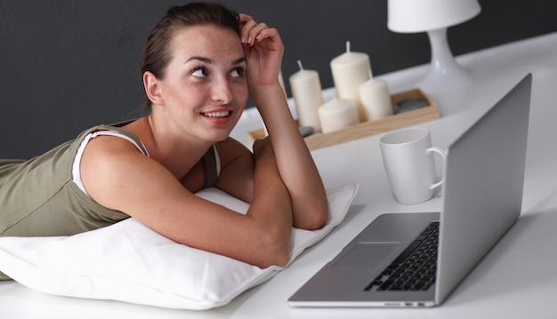 Foto eine junge frau, die auf dem fußboden mit einem laptop liegt