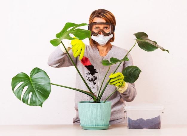 Eine junge Frau, die eine medizinische Maske und eine Schutzbrille trägt, schaufelt Schmutz