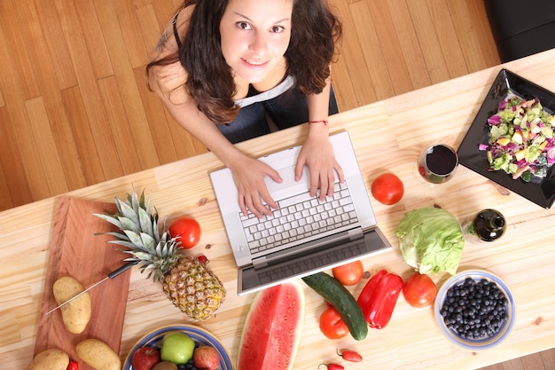 Eine junge Frau, die einen Laptop beim Kochen benutzt.