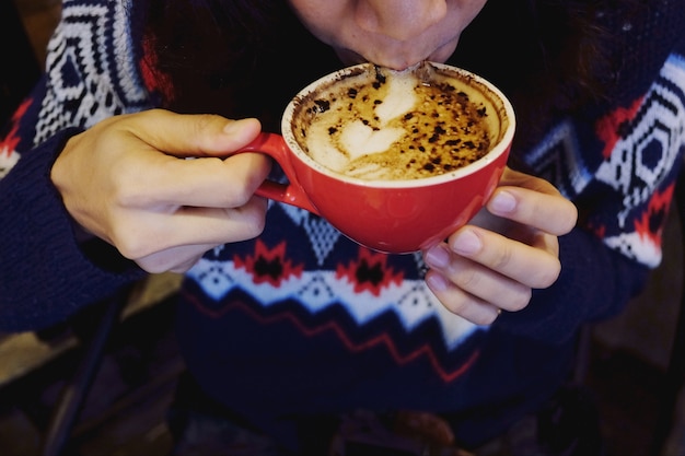 Eine junge frau, die einen roten tasse kaffee in ihren händen hält und es morgens trinkt