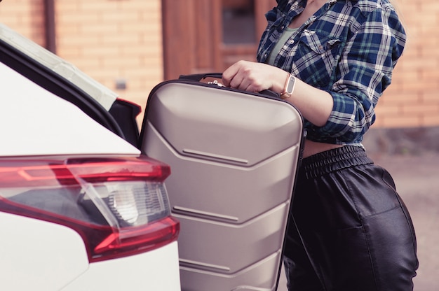 Eine junge Frau, die ihr Gepäck in den Kofferraum eines Autos steckt