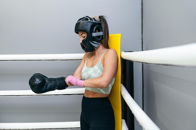 Eine junge Frau, die ihren Boxhandschuh an der Hand anlegt, bevor sie ihre Boxroutine im Fitnessstudio beginnt