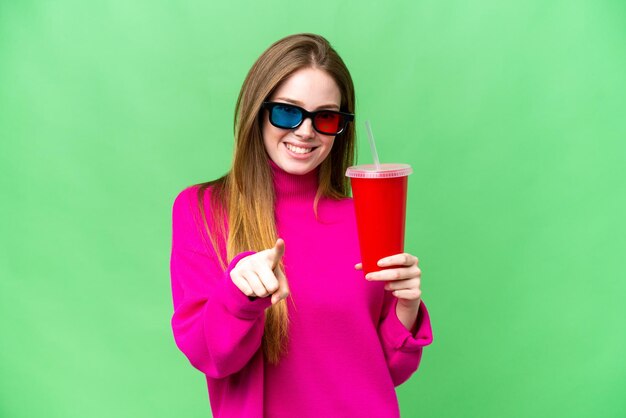 Eine junge Frau, die Limonade hält, während sie sich einen 3D-Film ansieht, zeigt mit einem selbstbewussten Ausdruck mit dem Finger auf Sie
