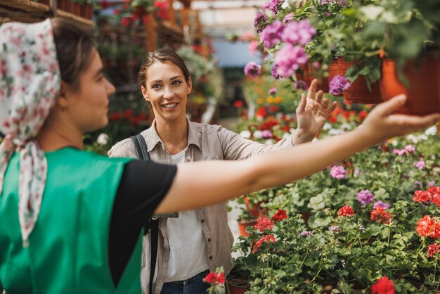 Eine junge Frau, die Pflanzen und Blumen von einer jungen Unternehmerin in einem Gartencenter auswählt und einkauft.