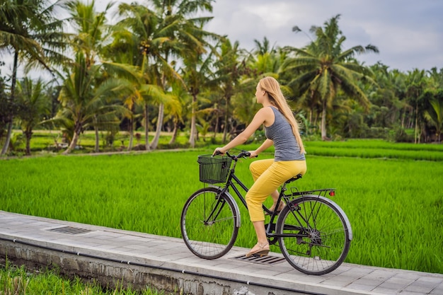 Eine junge Frau fährt Fahrrad auf einem Reisfeld in Ubud Bali Bali Travel Concept