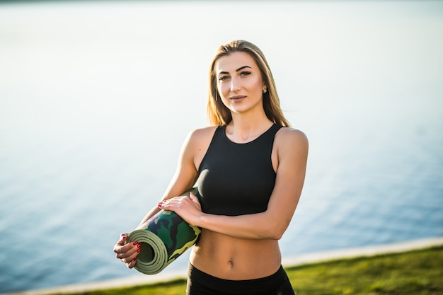 Eine junge Frau geht mit Yogamatte für ihr Training am Strand. Draussen.