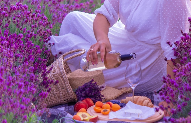 Eine junge Frau gießt Wein in ein Glas auf einem LavendelfeldNatur