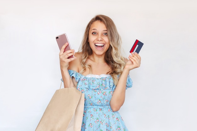 Eine junge Frau hält ein Kreditkartenhandy und eine Papiertüte in den Händen, um Einkäufe zu bezahlen