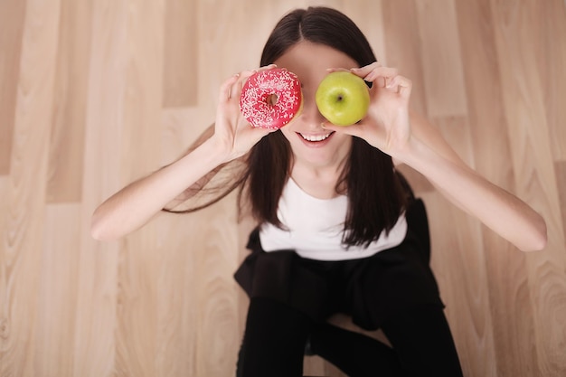 Eine junge Frau hält eine Pizza auf der Waage und trifft die Wahl zwischen einem Apfel und einem Donut