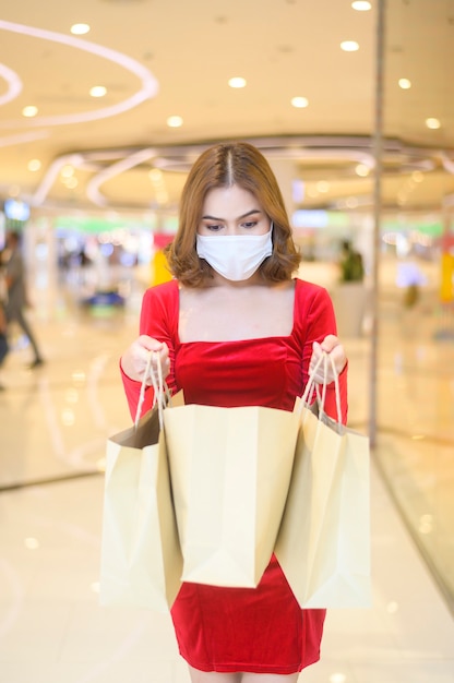 Eine junge Frau im roten Kleid mit Schutzmaske im Einkaufszentrum shopping