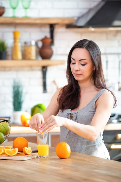 Eine junge Frau in einem grauen T-Shirt drückt eine frische Orange auf Fruchtsaft