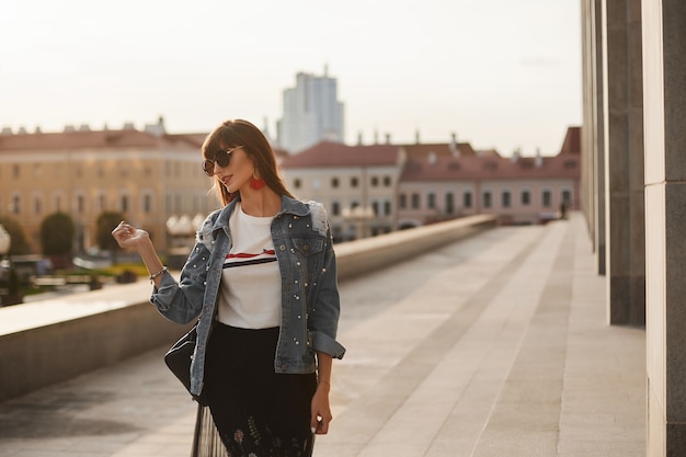 Foto eine junge frau in einem modischen sommeroutfit geht am sommertag auf der stadtstraße spazieren.