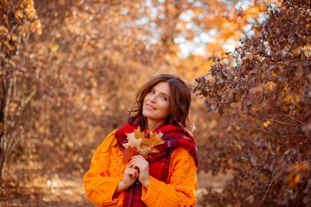 Eine junge Frau in einem orangefarbenen Pullover hüllt sich in einem Herbstpark in einen Schal