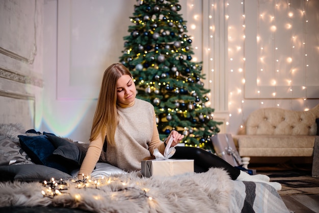 Eine junge Frau in einem Pullover mit langen schönen Haaren sitzt und lacht vor Weihnachtsgeschenken. Frohes Neues Jahr